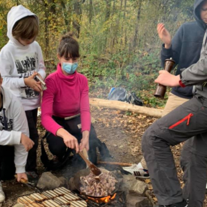 animatrice et enfants cuisant une poellée de champignons sur le feu de bois en école du dehors