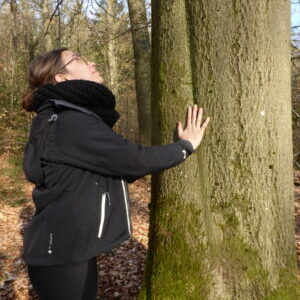 une femme pose ses mains sur un gros tronc de hêtre (Champlon)